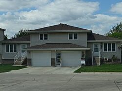 Image shows a modern two-story residential house with a garage, well-maintained lawn, and clear skies, representing home insurance coverage.