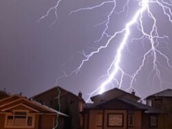 Lightning bolt striking roofs during storm for home insurance coverage; Norfolk Mutual Insurance offers reliable home protection.